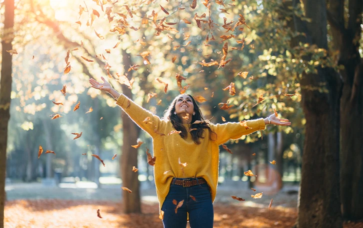 Eine Frau unter Baumen mit fallenden Blättern um sich herum